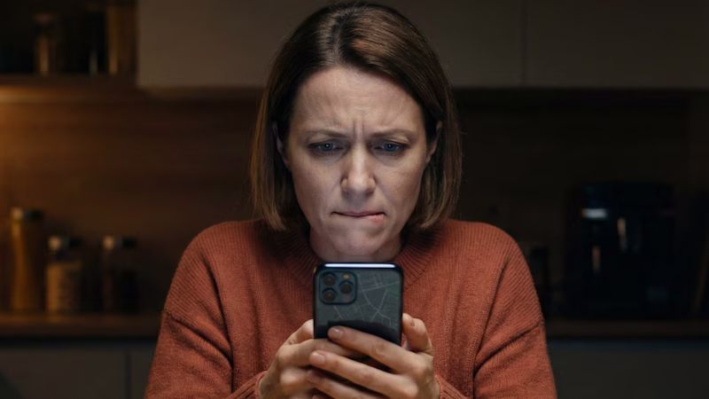 Madre mirando el móvil con ansiedad en la cocina.